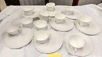 12 sets of white Royal Tuscan tea cups with matching biscuit plates, arranged on a table showing all pieces.