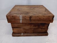 Front and side view of rustic wooden storage box showing weathered surface and metal latch on lid.