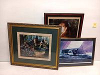 Three framed art prints: one of a quaint cottage, one of an Impressionist Renoir style painting of a woman, and one of a sailing scene artwork.