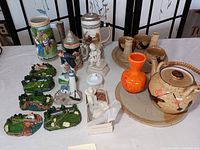 Photo showing golf-themed collectibles, beer steins, a ceramic teapot set, pottery pitchers, Clark Gable figurine, and monkey-shaped soaps