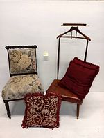 Photo of a floral upholstered occasional chair, mid century valet stand with leather seat and three red throw pillows.