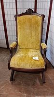 Front view of Victorian upholstered wooden rocking chair showing yellow fabric and carved wood details.