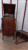 Victor Victrola phonograph housed inside wooden cabinet with doors closed, and the separate wooden wall hanging shelf on floor nearby.