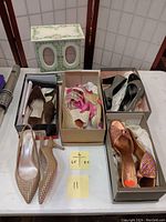 Overview photo showing five pairs of women's shoes of various sizes arranged on a table with boxes, and the vintage-style musical jewelry chest behind them.