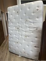 Photo of the double mattress standing upright showing a white, tufted fabric cover with decorative patterns.