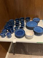 Full overview of all blue ceramic dishes and cups, pitchers, and covered containers on a table.