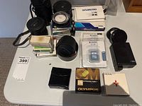 Photo showing multiple camera lenses in cases, Olympus manuals, and other accessories on table.