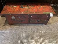 Full front view of the rectangular chest showing the reddish painted surface with colorful floral and bird designs. Two side-hinged doors and one upper drawer visible.