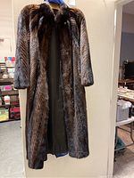 Full view of the front open fur coat hanging on a hanger against a door, showing length and dark inner lining.