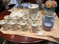 Full display of Mikasa Wildflower dishes with mugs, bowls, plates, cookie jar, small pitcher and decorative bowls on table.