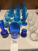 Photo showing full assortment of blue and clear glassware items including mugs, glasses, bowls, and decorative pieces arranged on a flat surface.