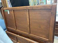 Back view of brown solid wood headboard and footboard panels with visible wood grain and rectangular insets.