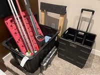 Overview of black heavy-duty storage bin filled with cleaning tools and next to black collapsible cart and low rolling cart