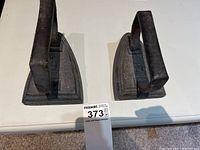 Photo of two vintage cast irons from top view, showing their triangular flat bases and iron handles on a white table.