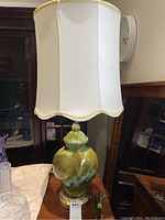 Full view of the MCM lamp with cream white fabric shade and ceramic glazed base in greens and browns