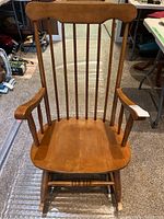 Front view of the wooden rocking chair showing slatted backrest, armrests, and seat.