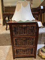 Wood side table with three wicker basket drawers and cream lampshade on top