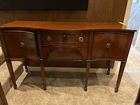 Full frontal view of the solid wood sideboard showing three sections: two curved door cabinets and a central drawer with brass round handles.