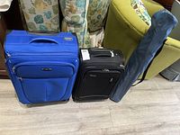 Blue soft-side suitcase, black soft-side suitcase, and folded camping chair in carry bag placed on floor