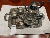 Full view of the complete silver-tone tea and coffee set on an ornate serving tray including pots, cream and sugar bowls, salt and pepper shakers.