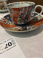 Close-up of one teacup and saucer showing detailed multicolor floral and geometric patterns with gold accents.