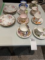 Lot overview showing eight teacups with matching saucers and several serving plates, all with floral motifs and gold trim.