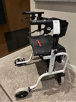 Front view of white metal rollator walker showing seat, backrest, hand brakes, and four wheels.
