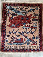 Overall view of the rectangular wool rug showing Afghanistan map in red center surrounded by military hardware motifs including tanks, helicopters, grenades, and missile launchers.