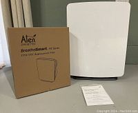 Air purifier next to boxed filter and manual on floor