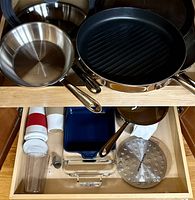 Overhead view of multiple stainless steel and nonstick All-Clad pans and lids in a drawer