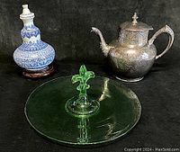 Photo of the blue and white porcelain wine bottle, Victorian silver plate teapot, and green Fostoria tidbit tray against black background.