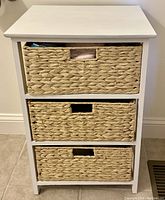 Storage basket chest with three woven wicker pull-out baskets, white painted wooden frame, shown with baskets partially pulled out.
