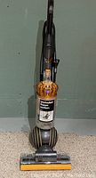 Full front view of upright vacuum on carpet showing cleaner head, ball base and handle