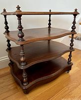 Front angled view of the four tier mahogany tea trolley showing the shape of scalloped shelves and turned spindle supports.