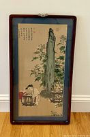 Full view of the framed Asian silk jacquard artwork showing the scene with child and adult next to blossom and stone slab.