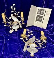 Two Baguès crystal and iron wall sconces with parrot motif displayed on purple cloth alongside a Baguès catalog sheet