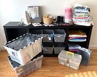Wide shot of the entire lot on and around a black shelving unit, showing the storage bins, fabrics, iron, thread, baskets, and various sewing notions.