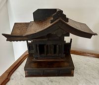 Front view of dark stained miniature Shinto shrine showing curved roof, gates, and base on a marble surface.