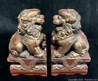 Front view of both red and gilt painted wood guardian lion statues on carved bases