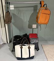 Full view of adjustable metal rolling clothing rack with the orange backpack and other bags arranged on and around it.