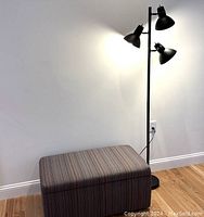 Set with striped upholstered bench and black three-head floor lamp against white wall on wood floor