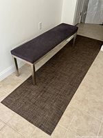 Angled view of Parsons bench on top of the dark basketweave rug, showing stainless steel base and charcoal fabric upholstery.