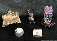 All items displayed on black background: paperweight on stand, landscape frame, Buddha figure, trinket box, carved button