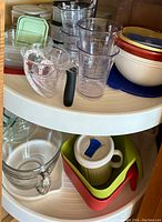 Top view of various storage containers including glass and plastic containers with lids, measuring cups, and mixing bowls on a lazy Susan shelf.