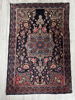 Full view of the rectangular Turkish wool rug featuring a dark background with floral and leafy motifs and a central medallion.