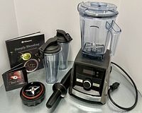 Overview of blender base with container mounted, two personal cups, tamper, blade assemblies and booklets