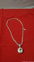 Full view of silver-tone chain necklace with round rhinestone pendant laid on a red fabric background.