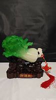 Photo of the front view of brand new Chinese cabbage decorative sculpture on a carved base with red tassel.