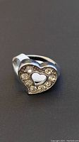 Front view of silver-tone heart-shaped ring with clear rhinestones, showing cut-out heart center and polished band.