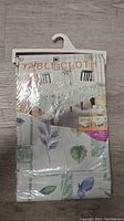 Front view of packaged tablecloth with printed leaf and flower design labeled 'TABLECLOTH'